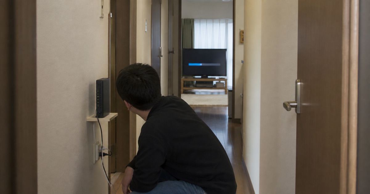 廊下のルーターと離れたテレビの更新状況を確認する様子
